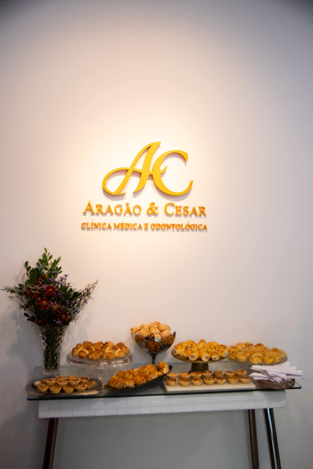 Letreiro dourado com o monograma Aragão & Cesar na parede da clínica